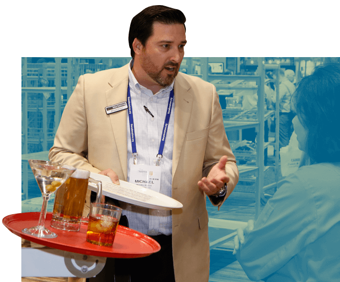 An male exhibitor holds a tray while speaking to a Show attendee.